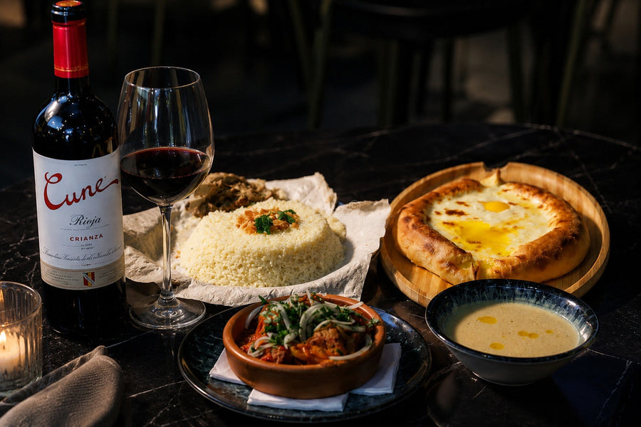 Botella de Rioja y copa de tinto junto a un khachapuri y otros platos georgianos en la mesa de un restaurante
